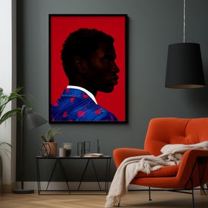 May include: A framed art print featuring a profile of a person with dark skin against a red background. The person wears a blue jacket with red heart-shaped designs and a white collar. The artwork hangs above an orange armchair.
