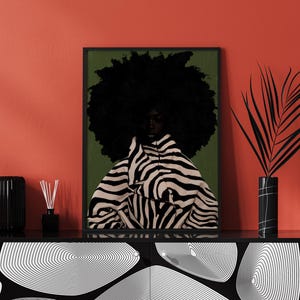 Op de afbeelding: Een ingelijste kunstdruk met een persoon met een grote afro en kleding met zebraprint. Het kunstwerk staat tegen een groene achtergrond en is zwart omlijst. De print wordt tentoongesteld op een zwarte kast met een rode muur op de achtergrond.