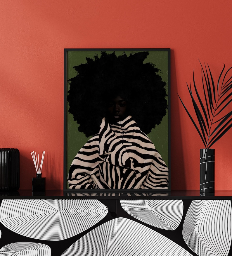 Op de afbeelding: Een ingelijste kunstdruk met een persoon met een grote afro en kleding met zebraprint. Het kunstwerk staat tegen een groene achtergrond en is zwart omlijst. De print wordt tentoongesteld op een zwarte kast met een rode muur op de achtergrond.