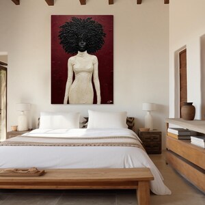 May include: An abstract painting of a woman with a large, textured afro and a cream-colored dress. The artwork hangs on a burgundy wall above a bed with white linens. The room has a minimalist design with wooden furniture and accents.