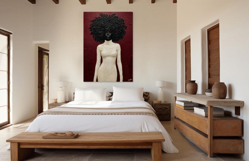 May include: An abstract painting of a woman with a large, textured afro and a cream-colored dress. The artwork hangs on a burgundy wall above a bed with white linens. The room has a minimalist design with wooden furniture and accents.