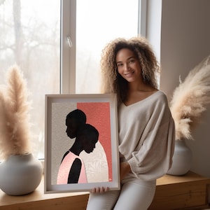 May include: A framed art print featuring a stylised illustration of two dark-skinned figures in profile against a split background of textured light grey and coral pink, with one figure wearing a light pink garment and a subtle leaf pattern.