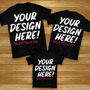 Puede incluir: Tres camisetas negras con el texto "YOUR DESIGN HERE! Blank Mock Up" impreso en blanco en cada camiseta.