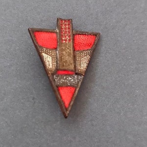 May include: A red, gold, and black enamel pin in the shape of a triangle with a geometric design.