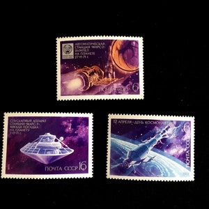 Puede incluir: Tres sellos postales soviéticos vintage que representan la exploración espacial. Los sellos presentan ilustraciones de naves espaciales sobre un fondo estrellado. El texto en los sellos dice "Автоматическая станция "Марс-2" Вымпел на планете 27-11-71", "Спускаемый аппарат станции "Марс-2" Мягкая посадка на планету 2-11-71", y "12 апреля - День космонавтики".