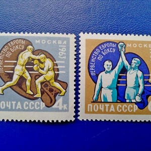 Könnte beinhalten: Zwei alte Briefmarken aus der Sowjetunion, die Boxkämpfe zeigen. Die Briefmarken sind blau und gelb mit dem Text "ПЕРВЕНСТВО ЕВРОПЫ ПО БОКСУ" und "ПОЧТА СССР" in kyrillischer Schrift. Die Briefmarken stammen aus den Jahren 1963 und 1967.