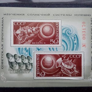 Può includere: Due francobolli sovietici vintage con illustrazioni di veicoli spaziali. Il francobollo superiore mostra un veicolo spaziale con il testo "CCCP" e "ПОЧТА 1972" e le parole "ВЕНЕРА-8" e "50". Il francobollo inferiore mostra un veicolo spaziale con il testo "CCCP" e "ПОЧТА 1972" e le parole "МАРС-3".