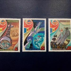 May include: Three vintage Soviet postage stamps depicting space travel. The stamps feature a rocket, a space station, and astronauts in space suits. The stamps are from 1981 and have the text "Международные полеты в космос" which translates to "International Flights in Space".