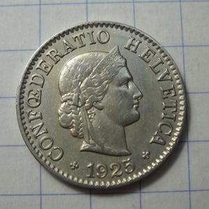 Op de afbeelding: Een zilveren munt met het profiel van een vrouw met een lauwerkrans. De munt is gegraveerd met "CONFOEDERATIO HELVETICA" en het jaar "1925". De munt heeft een gekartelde rand. Raster achtergrond.