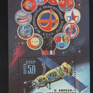 May include: A postage stamp featuring a spacecraft with solar panels, a yellow and green body, and the text "CCCP 50". The stamp also includes various circular emblems and the text "12 April - Cosmonautics Day".
