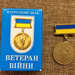 May include: A blue box with the text "Нагрудний знак ВЕТЕРАН війни" and a gold medal with a woman holding a torch and the text "Ветеран війни" on it. The medal is on a blue and yellow ribbon.