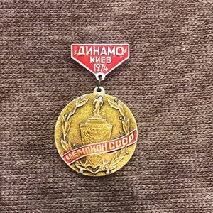 May include: A gold and red medal with a laurel wreath and a trophy. The medal has the text "Чемпион СССР" and "ДИНАМО КИЕВ 1974" on it.