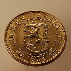 May include: A gold-colored coin with the text "SUOMEN TASAVALTA" around the edge. The coin features a lion rampant in the center, with the year "1956" below. The coin has a detailed, textured design.