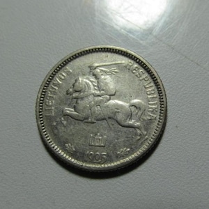 May include: A silver coin featuring a knight on horseback with a sword, a symbol of Lithuania. The coin has the inscription "LIETUVOS RESPUBLIKA" and the year "1995". The coin's edge has a textured pattern.