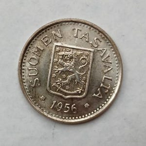May include: A silver coin with the text "SUOMEN TASAVALTA" around the edge. The coin features a shield with a lion rampant and the year "1956" at the bottom. The coin has a circular shape and a detailed design.