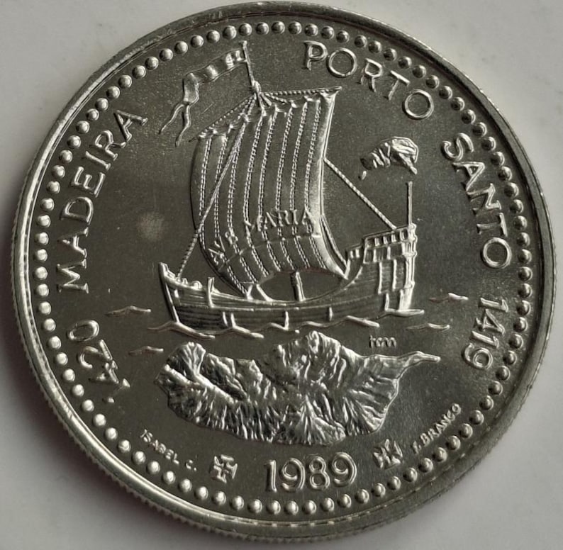 Puede incluir: Moneda de plata con una representaci&oacute;n detallada de un velero con la palabra "MARIA" en la vela, sobre un fondo de una isla monta&ntilde;osa. La moneda est&aacute; inscrita con "MADEIRA PORTO SANTO 1419" y el a&ntilde;o "1989".