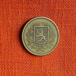 May include: A silver coin featuring a coat of arms with a lion and the numbers "1937". The coin is set against a textured orange background.
