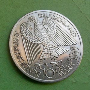 Può includere: Moneta d'argento da 10 marchi tedeschi del 1987. La moneta presenta un'aquila dettagliata con le ali spiegate, con le parole "BUNDESREPUBLIK DEUTSCHLAND" e "10 DEUTSCHE MARK" incise.