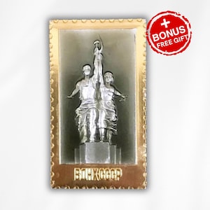 May include: A gold-colored metal frame with a silver-colored image of a statue of two figures holding a hammer and sickle. The statue is set against a dark gray background. The frame has a gold-colored border with a repeating pattern of small circles. The text "CCCP" is printed in gold letters at the bottom of the frame.
