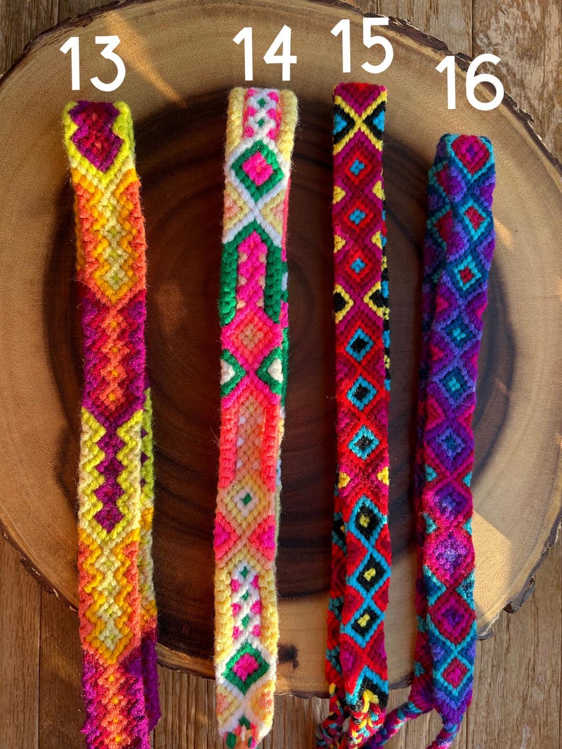 K&ouml;nnte beinhalten: Vier farbenfrohe gewebte Freundschaftsarmb&auml;nder mit geometrischen Mustern. Die Armb&auml;nder weisen lebendige Farbt&ouml;ne von Gelb, Orange, Rosa, Rot, Blau und Lila auf. Jedes Armband hat ein einzigartiges Design, das komplizierte Kn&uuml;pftechniken zeigt. Die Armb&auml;nder werden auf einer Holzoberfl&auml;che pr&auml;sentiert.