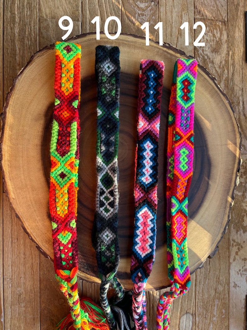 K&ouml;nnte beinhalten: Vier farbenfrohe gewebte Freundschaftsarmb&auml;nder mit komplizierten geometrischen Mustern. Die Armb&auml;nder weisen leuchtende Farbt&ouml;ne von Rot, Orange, Gr&uuml;n, Pink, Blau und Schwarz auf. Jedes Armband wird auf einer Holzscheibe mit den Nummern 9, 10, 11 und 12 dar&uuml;ber pr&auml;sentiert.