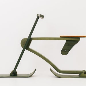 以下が含まれることがあります： 緑色の塗装が施された木製のおもちゃのそりで、オレンジ色の座席が付いています。そりはハンドルと2本のスキーが付いています。