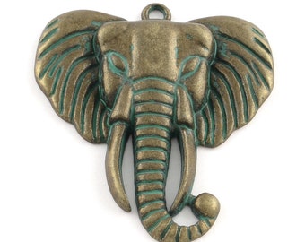 May include: A bronze-colored elephant head pendant with a loop for hanging. The pendant has a distressed finish with green accents, highlighting the details of the elephant's face, ears, and tusks. The elephant's head is centered, with a detailed trunk and large ears.