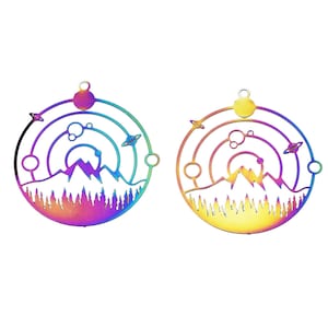 May include: Two circular metal pendants with a mountain and space-themed design. The pendants feature a rainbow gradient of colors. The design includes mountains, trees, planets, and a sun or moon. Each pendant has a small loop at the top for hanging.