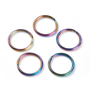 May include: Five iridescent key rings arranged on a white background. The rings display a spectrum of colors, including gold, purple, and blue. Each ring has a split for attaching keys or other items. The key rings are made of metal.