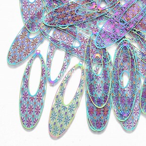 May include: A collection of iridescent oval-shaped metal earring components. Each component features a floral pattern within a filigree design, with a light blue outline. The components are scattered on a white surface.