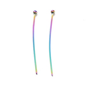 May include: A pair of iridescent earrings with a ball at the top and a long, curved, thin post. The earrings have a rainbow color scheme, with hues of purple, blue, green, and yellow. The earrings are displayed against a white background.