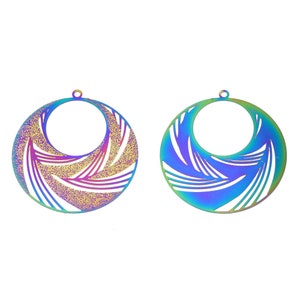 May include: Two iridescent, circular pendant charms. Each charm features a large central opening and a detailed, swirling pattern cut into the metal. The colors shift from purple to blue and green, creating a vibrant, eye-catching effect. The charms have small loops at the top for hanging.