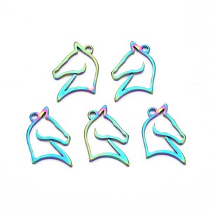 May include: Five iridescent horse head charms. Each charm is a cutout of a horse's head profile, featuring a loop at the top for attachment. The charms display a spectrum of colors, including blues, greens, and purples, creating a shimmering effect. They are set against a white background.