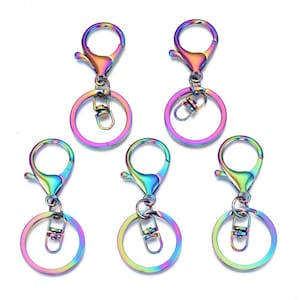 May include: Five iridescent keychains with lobster claw clasps and circular key rings. The keychains display a spectrum of colors, including purple, green, and gold. The key rings have a small clasp for attaching keys or charms.