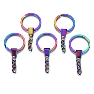 May include: Five iridescent keychains with round rings, rectangular connectors, and short chain links. The keychains display a spectrum of colors, including purple, blue, green, and gold, against a white background. These keychains are suitable for various crafting projects.