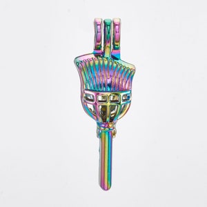 May include: A metallic rainbow-colored paint brush pendant. The pendant features a brush head with bristles, a handle, and a loop at the top for hanging. The iridescent finish reflects a spectrum of colors, including blues, greens, and purples.