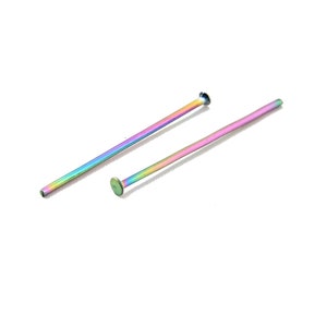 May include: Two iridescent rainbow-colored straight pins. One pin has a flat, round head, and the other has a slightly larger, flat head. The pins are set against a white background.