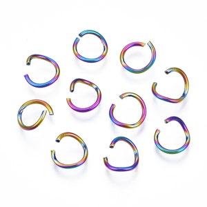 May include: A collection of ten rainbow-colored, open-ended rings. The rings are curved and have a metallic sheen, displaying a spectrum of colors including blue, purple, green, and yellow. They are arranged on a white surface, suggesting a jewelry or craft supply.