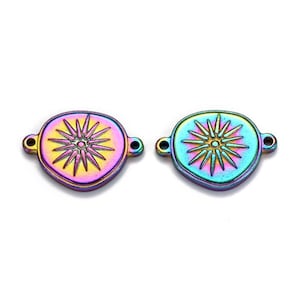 May include: Two iridescent metal charms with a starburst design. Each charm is oval-shaped with a central starburst pattern and two small loops for attaching to jewelry. The charms display a range of colors, including purple, blue, and gold.