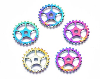 May include: Five iridescent metal gear charms with a rainbow finish. Each gear has a circular shape with a central hole and multiple teeth around the edge. The colors shift from blue to purple to yellow.