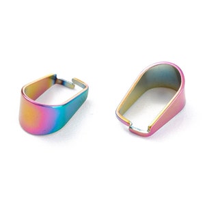 May include: Two iridescent metal pendant bails. The bails have a rainbow finish with colors of blue, purple, and gold. The bails are oval-shaped with a small opening at the top for attaching to a chain or cord.