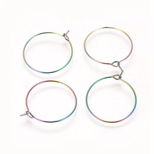 May include: Four iridescent hoop earrings. Each earring is a thin, circular wire with a hook closure. The earrings display a spectrum of colors, including blues, greens, and purples, creating a rainbow effect. The earrings are set against a white background.