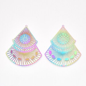 May include: Two iridescent fan-shaped pendants with intricate cut-out designs. Each pendant features a central circular pattern, radiating lines, and teardrop-shaped accents. The pendants are made of a shiny, metallic material and are displayed against a white background.