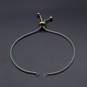 May include: A multi-colored adjustable bracelet with a chain-link design. The bracelet features a sliding knot closure with two small, iridescent beads. The metal has a rainbow finish, with hues of purple, green, and gold.
