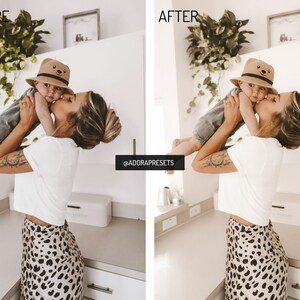 May include: A woman in a white t-shirt and leopard print skirt holds a baby wearing a brown hat with a bear face on it. The baby is wearing a gray shirt and jeans. The woman is kissing the baby on the cheek. The image is taken in a kitchen with white cabinets and a white countertop.