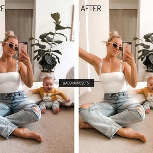 May include: A woman and a baby are sitting on the floor. The woman is wearing a white tank top with black straps that say "Make a Wish" and blue jeans. The baby is wearing a yellow sweater with a white bunny on it. The woman is holding a phone and taking a selfie. The background is a light brown wall with a plant in a pot.