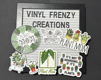 May include: A collection of colorful plant-themed stickers with the text "PLANT MOM" and other plant-related phrases. The stickers feature various plant illustrations, including cacti, succulents, and tropical leaves. The stickers are displayed on a gray felt letter board.