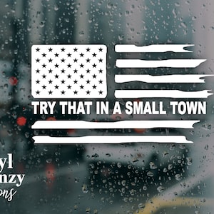 Könnte beinhalten: Weißer Vinyl-Aufkleber mit einem abgenutzten amerikanischen Flaggenmotiv und dem Text "TRY THAT IN A SMALL TOWN" darunter.