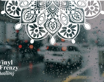 May include: A white vinyl decal featuring a symmetrical mandala pattern with intricate floral and geometric shapes. The decal is displayed against a rainy window background with blurred city traffic lights and the text Vinyl Frenzy Creations.
