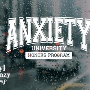 Op de afbeelding: Witte vinyl sticker met het woord "ANXIETY" in een universiteitslettertype, gebogen boven "UNIVERSITY HONORS PROGRAM". De sticker bevat ook de tekst "Vinyl Frenzy Creations" in een scriptlettertype. De achtergrond is een met regen beslagen raam.